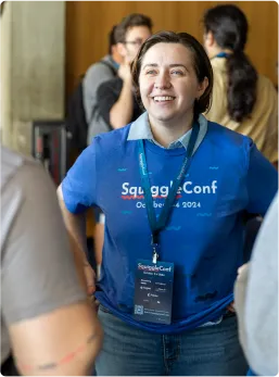 A smiling woman in a SquiggleConf 2024 shirt and badge